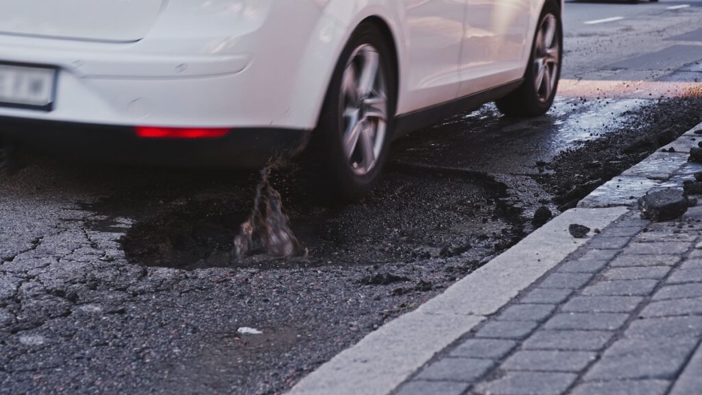 Wheels weren't made to take in the force when tyres hit the hard edges of potholes because they will bend or crack Vehicles,Driving,Over,Deep,Large,Erosion,Hole,In,City,Street