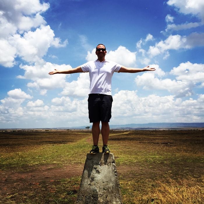 man standing on border marker between kenya's maasai mara and tanzania's serengeti